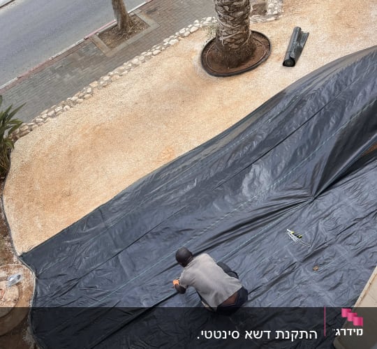 אדם פורש יריעת פלסטיק שחורה בגינה